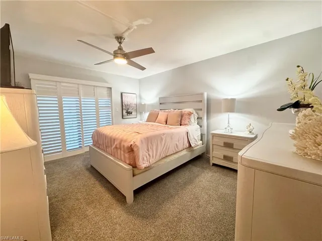 Bedroom featuring carpet and a ceiling fan.  Behind the plantation shutters is a private balcony with views of Gulf & Bay