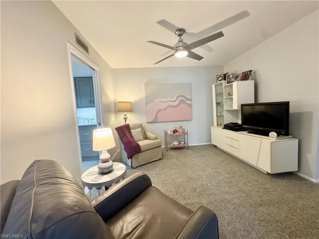 Den with carpet floors, a ceiling fan, and vaulted ceiling