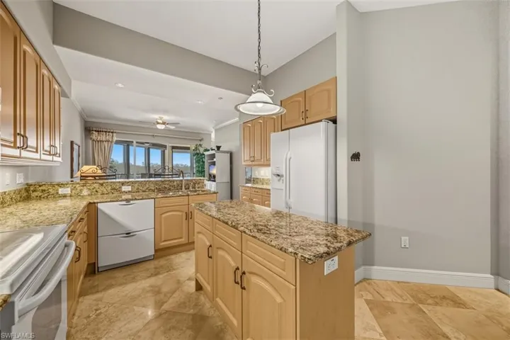 Kitchen with white appliances, decorative light fixtures, light stone countertops, ornamental molding, and a center island
