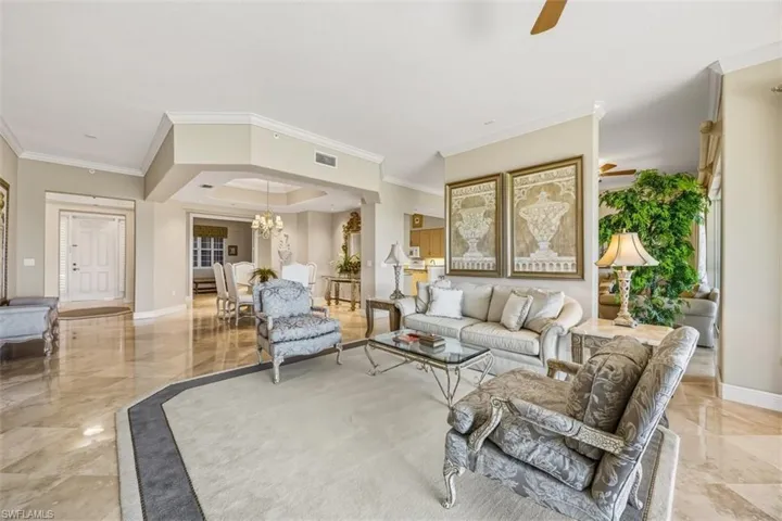 Living room with a tray ceiling, a chandelier, crown molding, a ceiling fan, and light marble finish flooring