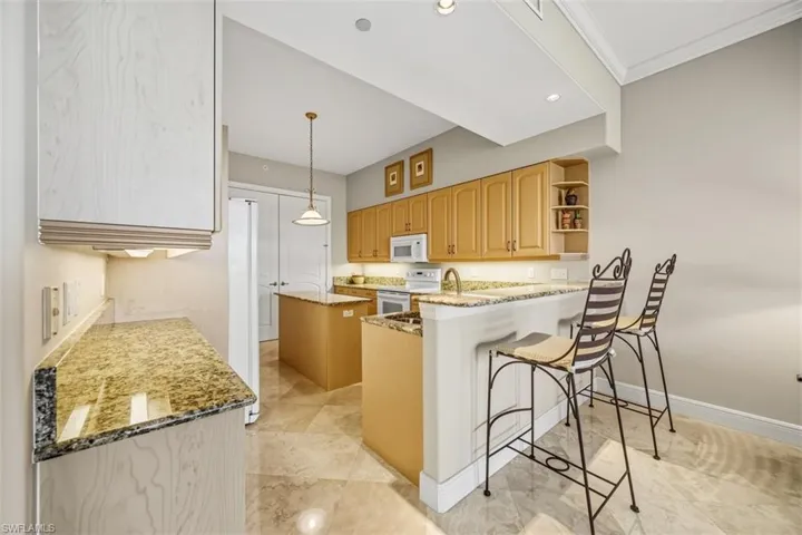 Kitchen with light stone counters, a kitchen island, a kitchen bar, white appliances, and open shelves