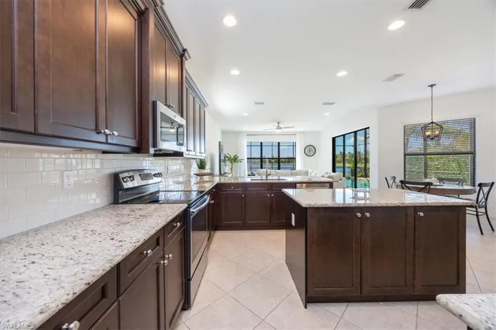 Kitchen featuring appliances with stainless steel finishes, decorative backsplash, dark brown cabinets, light tile patterned floors, and recessed lighting