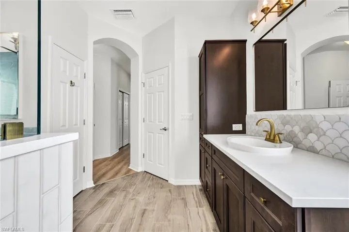The primary bathroom showcases beautiful cabinetry, detailed tilework, and elegant gold faucets.