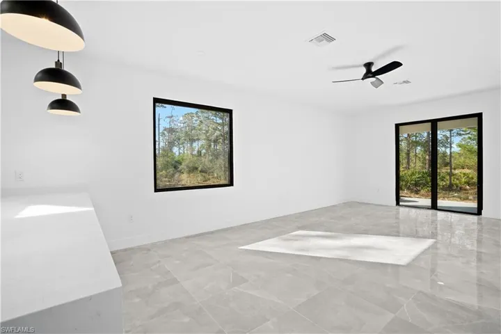 Spacious room featuring large format tile flooring, black framed window, sliding glass doors, contemporary ceiling fan, and built-in pendant lighting