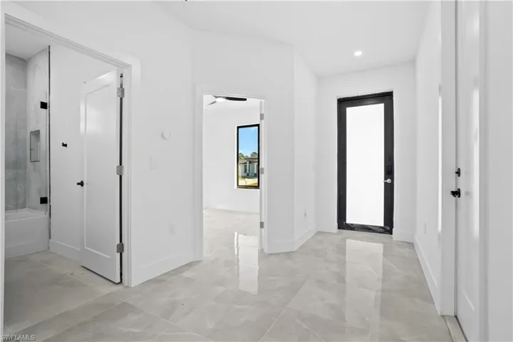 Bright hallway featuring large format grey tile flooring, recessed lighting, a modern black-framed full-light door, and a full bathroom with a tub and glass shower enclosure