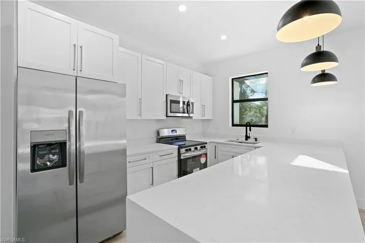 Modern kitchen featuring white shaker cabinetry, stainless steel appliances, white countertops, and contemporary pendant lighting