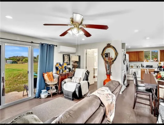 Living room featuring stacked washer / drying machine, an AC wall unit, ceiling fan, and plenty of natural light