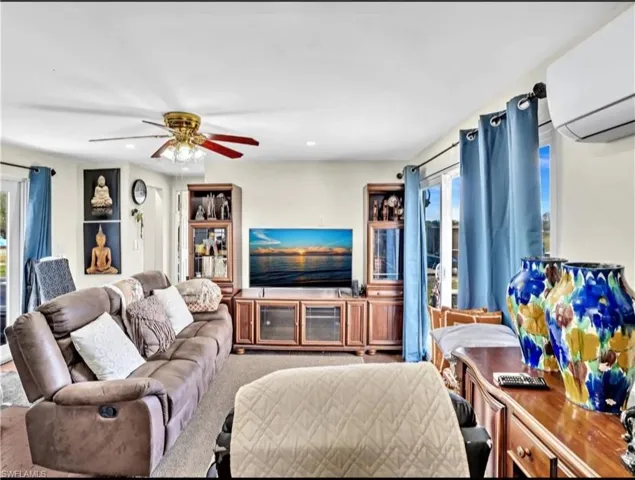 Living room featuring a wall unit AC, carpet flooring, and ceiling fan