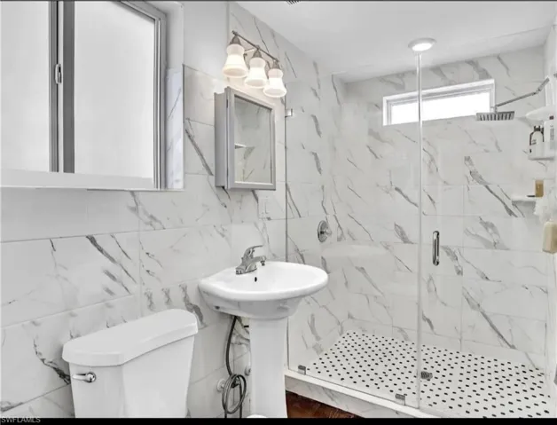 Bathroom featuring sink, toilet, a shower with door, and tile walls