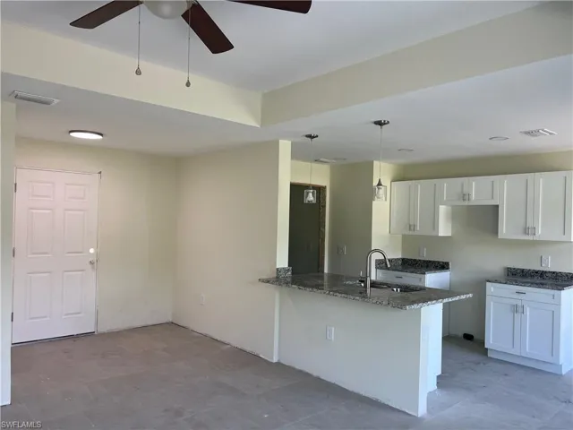 Kitchen with sink, tile patterned flooring, hanging light fixtures, white cabinetry, and ceiling fan
