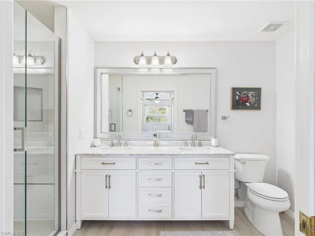 Full bath featuring double vanity, a shower stall, light wood-type flooring, and ceiling fan
