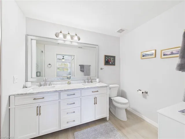 Full bathroom with double vanity, light wood finished floors, a shower stall, and a ceiling fan