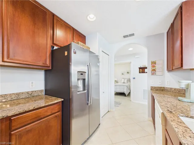 Kitchen featuring light stone countertops, stainless steel refrigerator with ice dispenser, light tile patterned floors, arched walkways, and recessed lighting