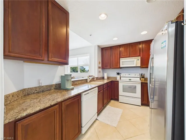 Kitchen with white appliances, light stone countertops, light tile patterned floors, recessed lighting, and a textured ceiling