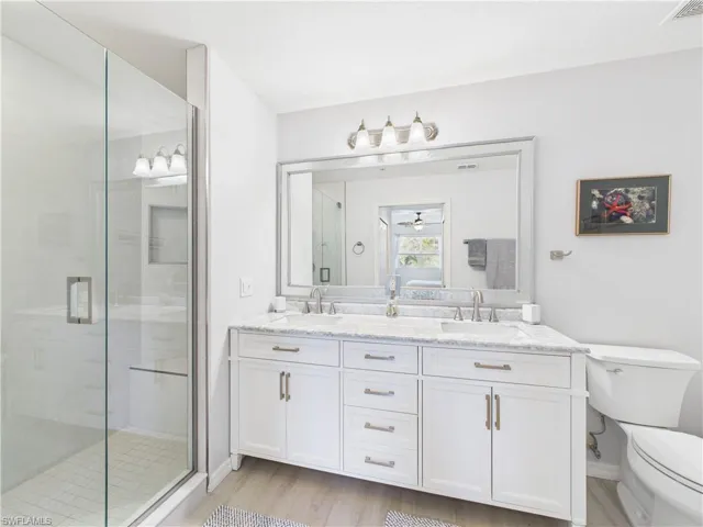 Full bath featuring double vanity, a shower stall, light wood-style flooring, and a ceiling fan