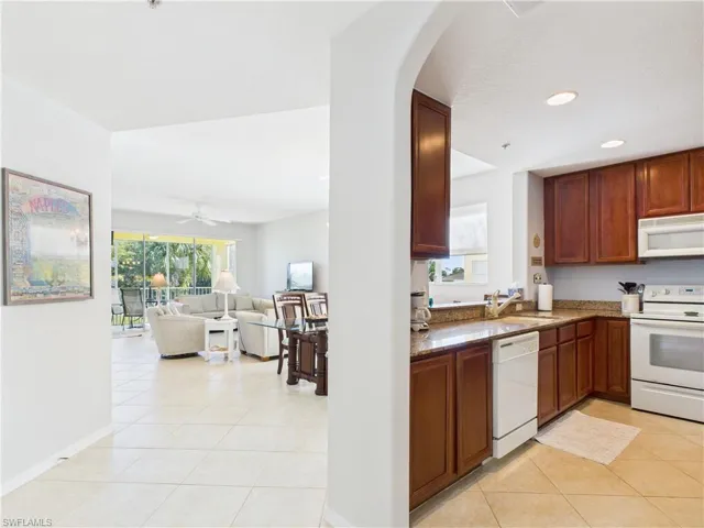 Kitchen with white appliances, dark stone counters, light tile patterned flooring, open floor plan, and a ceiling fan