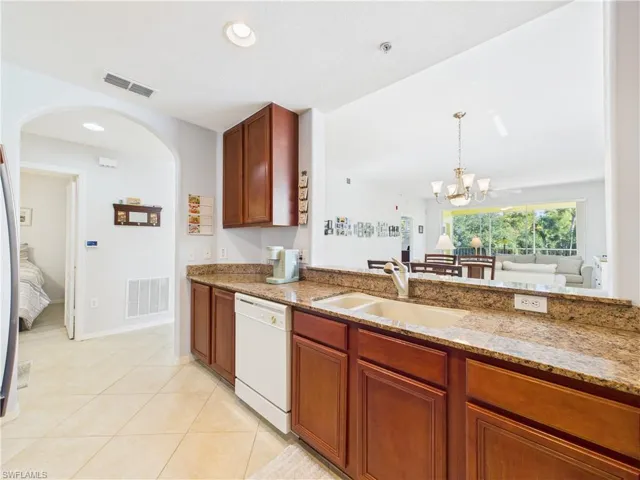 Kitchen with light stone countertops, white dishwasher, light tile patterned floors, arched walkways, and a chandelier
