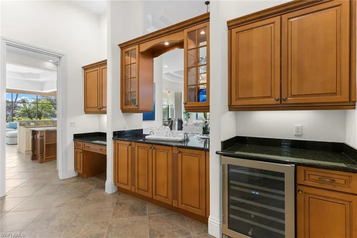 Bar area with wood finish cabinetry, wine cooler, glass insert cabinets, dark stone countertops, and healthy amount of natural light