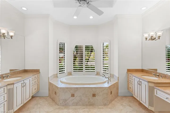 Bathroom with two vanities, a chandelier, ornamental molding, a bath, and a ceiling fan
