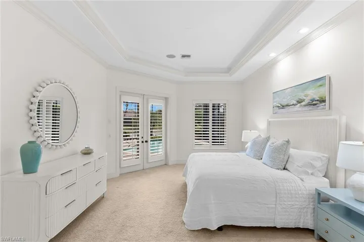 Bedroom with french doors, access to outside, light colored carpet, a tray ceiling, and crown molding