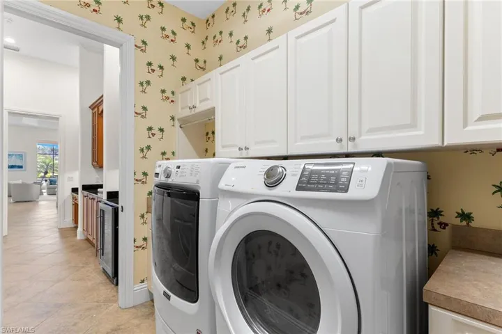 Laundry area with beverage cooler, cabinet space, wallpapered walls, washer and clothes dryer, and light tile patterned flooring
