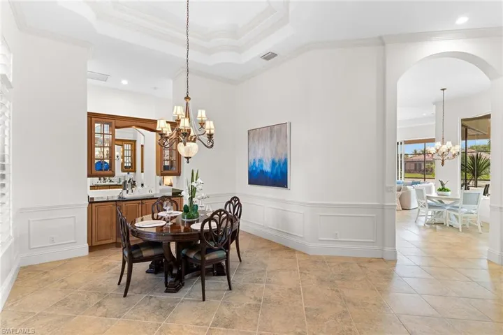 Dining area featuring suspended lighting, arched walkways, crown molding, and a wainscoted wall