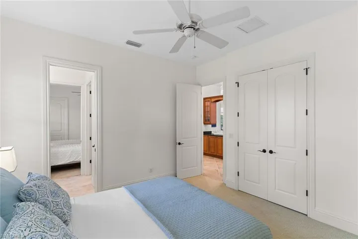 Bedroom with connected bathroom, light colored carpet, a closet, and a ceiling fan