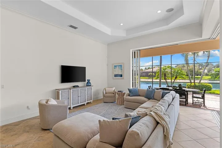 Living area with ornamental molding, recessed lighting, and a raised ceiling