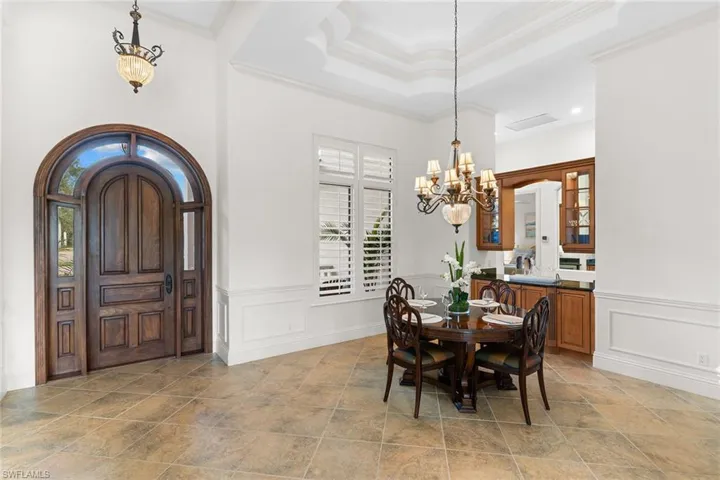 Dining room with suspended lighting, arched walkways, ornamental molding, a raised ceiling, and light stone finish floors