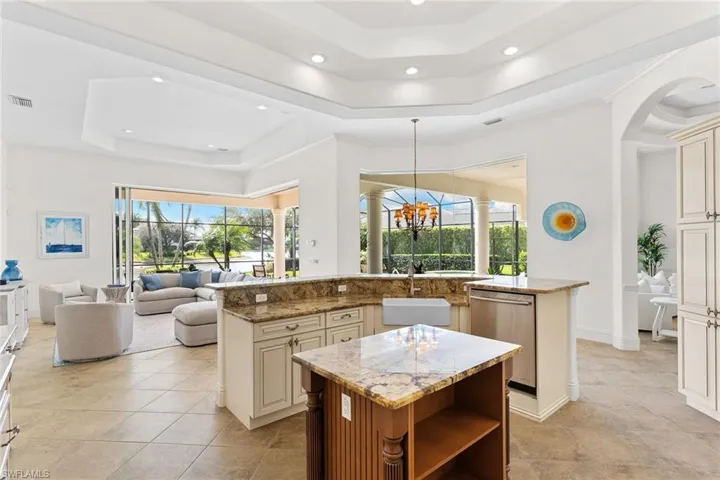 Dual tone kitchen with light stone counters, a tray ceiling, stainless steel dishwasher, open floor plan, and suspended lighting