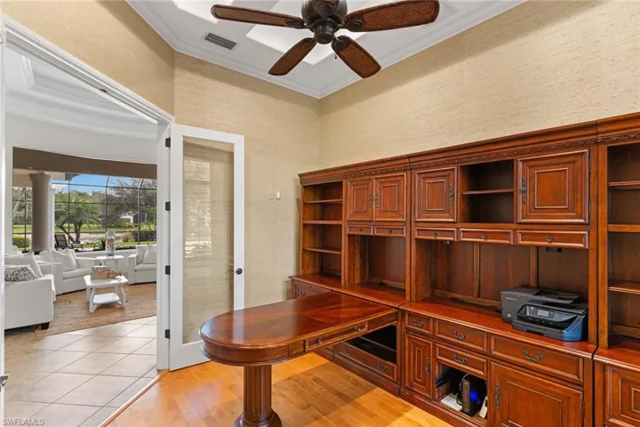 Office with light wood finished floors, ornamental molding, a ceiling fan, wallpapered walls, and a high ceiling