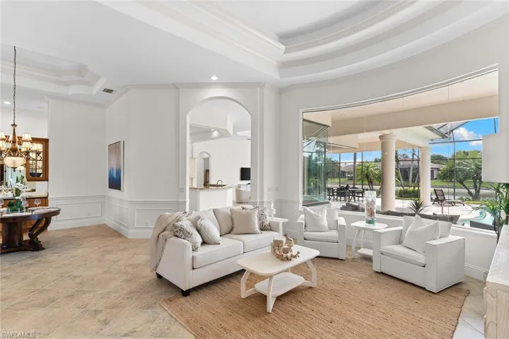 Living room featuring crown molding, suspended lighting, a raised ceiling, a wainscoted wall, and a decorative wall