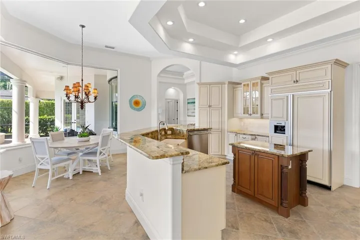 Kitchen with paneled built in fridge, light stone countertops, arched walkways, a chandelier, and dual tone cabinets