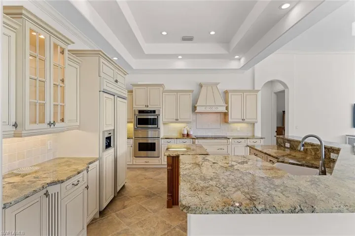Kitchen featuring cream cabinetry, backsplash, arched walkways, light stone counters, and a raised ceiling
