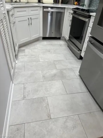 Kitchen with stainless steel appliances, white cabinetry, and light stone counters