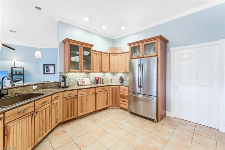 Kitchen featuring backsplash, hanging light fixtures, stone countertops, sink, and stainless steel fridge