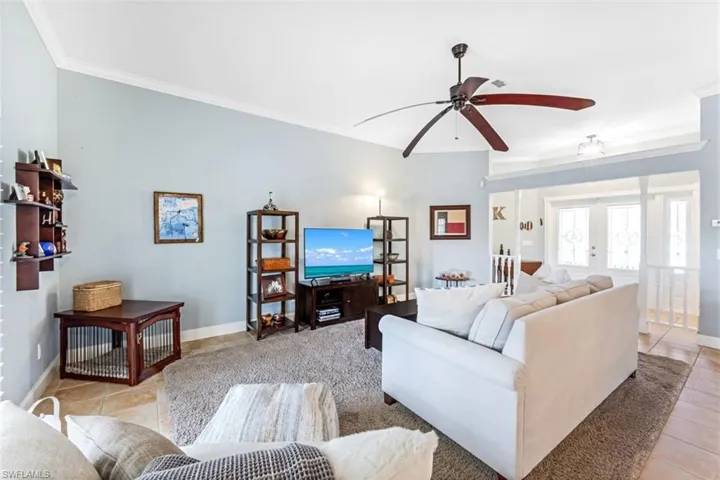 Living room with ceiling fan, light tile patterned floors, ornamental molding, and french doors