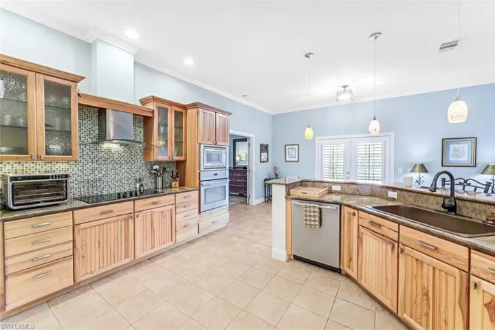 Kitchen with backsplash, wall chimney exhaust hood, hanging light fixtures, appliances with stainless steel finishes, and sink