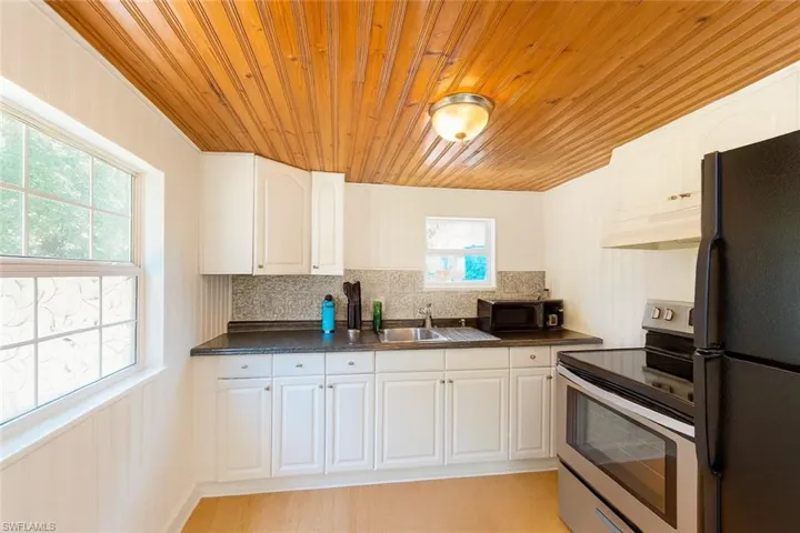 Kitchen featuring black appliances, dark countertops, wooden ceiling, tasteful backsplash, and under cabinet range hood