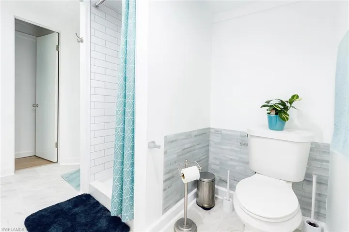 Bathroom with a shower stall, light tile patterned flooring, tile walls, and wainscoting