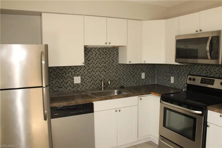 Kitchen with stainless steel appliances, sink, tasteful backsplash, and white cabinets