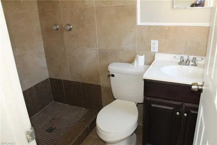 Bathroom featuring tile walls, a tile shower, vanity, and toilet