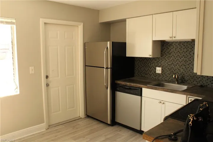 Kitchen with light hardwood / wood-style floors, white cabinetry, sink, and stainless steel dishwasher