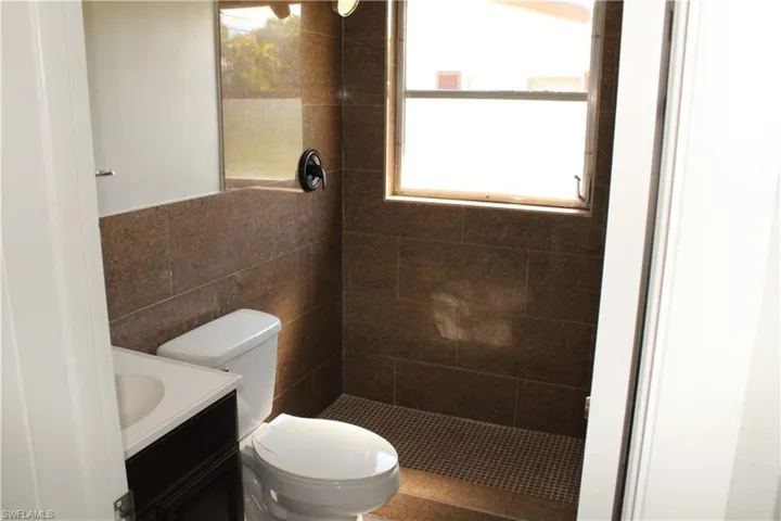 Bathroom featuring tiled shower, vanity, toilet, and tile walls