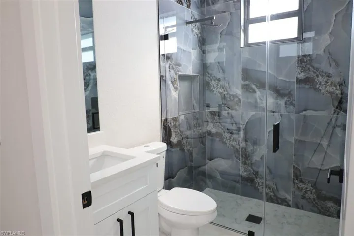 Full bath with a marble finish shower, vanity, and a textured wall