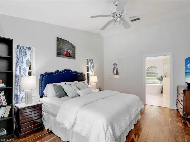 Bedroom with wood finished floors, vaulted ceiling, ceiling fan, and ensuite bathroom