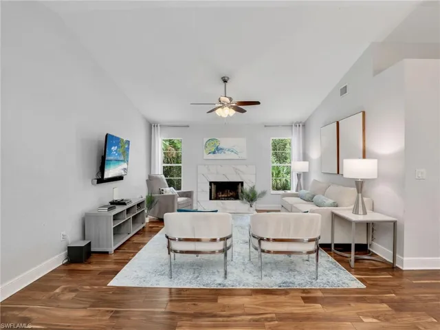 Living room with vaulted ceiling, ceiling fan, wood finished floors, and a fireplace