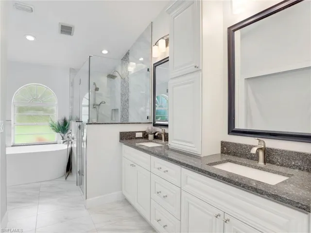 Full bathroom with marble finish flooring, a shower stall, double vanity, a freestanding bath, and recessed lighting