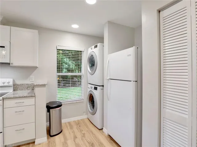 Laundry room with stacked washer / dryer, light wood-type flooring, and recessed lighting