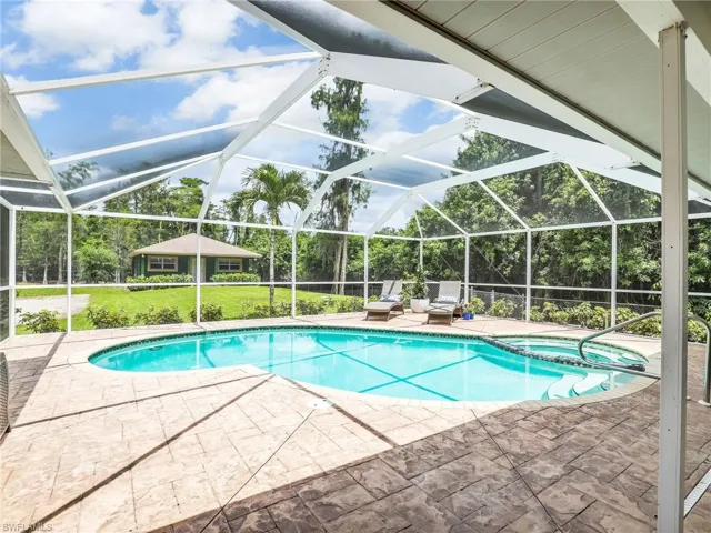 View of swimming pool featuring a patio area, a pool with connected hot tub, a yard, a lanai, and view of scattered trees